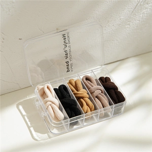 Five elastic hair ties in neutral tones stored in a transparent organizer box