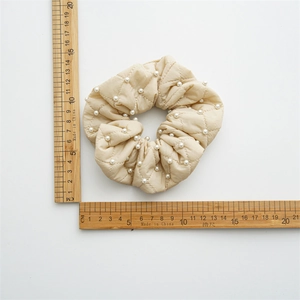 Top view of cream quilted scrunchie with pearls showing 12cm diameter on wood rulers