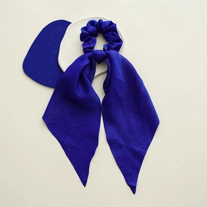 Detail of royal blue satin scrunchie with long ribbon tails on minimalist background