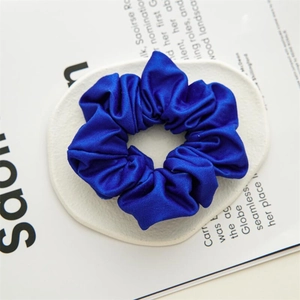 Détail d'un chouchou large en satin bleu roi avec texture soyeuse sur un support blanc