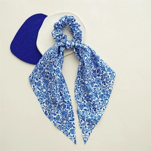 Close-up of blue floral satin scrunchie with long streamers on a minimalist background