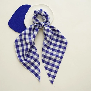 Detail of blue and white gingham hair scrunchie with long ribbon on a beige surface