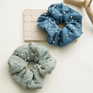 Detailed view of quilted velvet hair scrunchies in blue and green with pearl accents