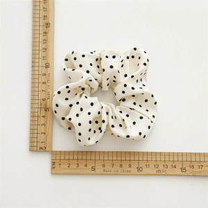 Chouchou en satin blanc à pois noirs, montrant un diamètre de 11cm sur fond blanc