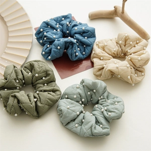 Close-up of quilted velvet scrunchies in four colors with elegant pearl embellishments