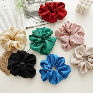 Set of 7 colorful satin silk scrunchies arranged on a warm aesthetic background