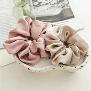 Set of two elegant satin scrunchies in rose pink and creamy white displayed on a ceramic dish