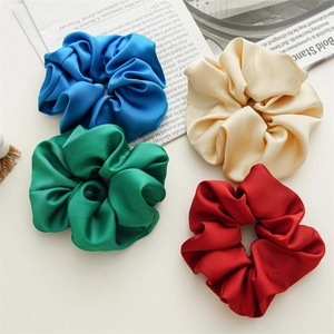 Detailed view of four satin silk hair scrunchies in blue, beige, green, and dark red colors