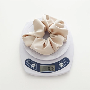 Detail showing a cream satin scrunchie weighing 10.8g on a digital scale for size reference