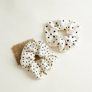 Vue détaillée de deux chouchous en satin blanc à pois noirs sur un tissu de lin