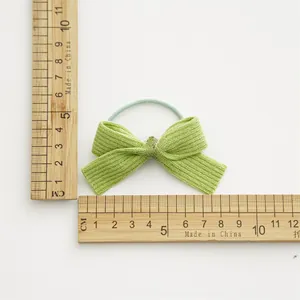 Detailed view of green bow hair tie with knitted texture and ruler for size measurement
