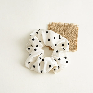 Détail d'un chouchou en satin blanc à pois noirs avec une texture de tissu doux