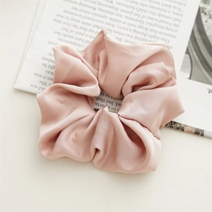 Close-up of wide satin scrunchie in dusty rose with elegant folds and silk texture