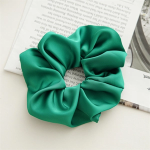 Detailed view of an emerald green satin scrunchie with a glossy silk texture for hair