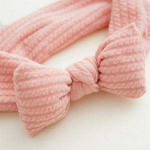 Détail d'un bandeau en maille rose bébé montrant la texture côtelée et un nœud papillon
