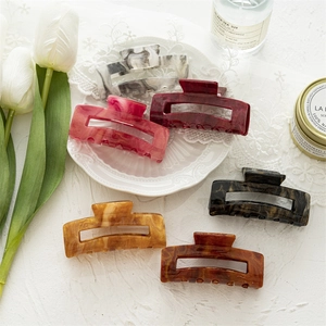 Set of six colorful marble pattern acrylic hair claws displayed with tulips
