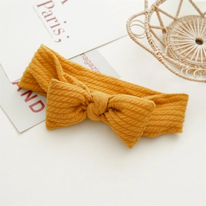 Gros plan du bandeau bébé en tricot jaune gingembre avec nœud et maille torsadée