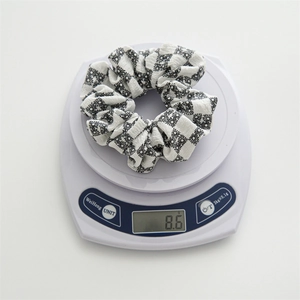 Detailed view showing the 8.6g lightweight checkered daisy fabric scrunchie on a scale