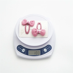 Set of two pink knitted bow hair clips for kids on a scale weighing 10.0g