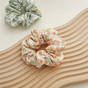 Dettaglio di elastici scrunchie a fiori arancioni e blu su vassoio in legno ondulato