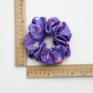 Detail view of purple satin scrunchie with colorful heart patterns next to a metric ruler
