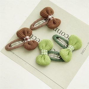 Detail view of four pieces of knitted bow hair clips in green and brown on a card