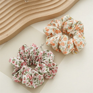 Dettaglio di elastici scrunchies in chiffon floreale nei toni arancione e rosa su vassoio