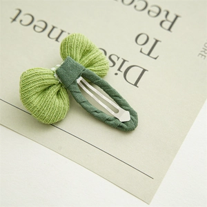 Detailed view of a green knitted bow hair clip on a minimalist aesthetic display card