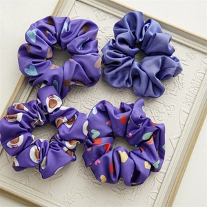 Detail of four purple satin hair scrunchies with heart patterns on a white frame