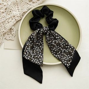 Dettaglio di uno scrunchie in raso nero con nastro floreale su piatto ceramico