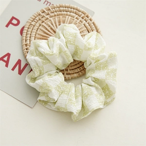 Détail d'un chouchou à fleurs vert clair en tissu seersucker sur un tapis tressé