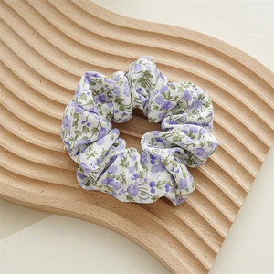 Dettaglio di scrunchie in chiffon a fiori viola su un vassoio di legno naturale