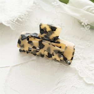 Detailed view of square tortoise shell acrylic hair claw on a decorative white stone base