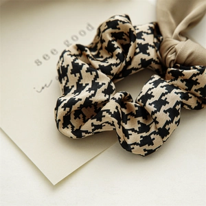 Detail of houndstooth silk scrunchie with a long khaki ribbon and elegant texture