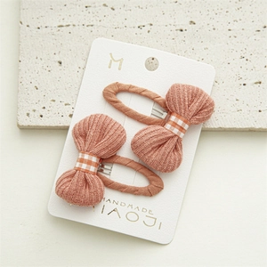Detail of two handmade orange knit bow hair clips on a white presentation card