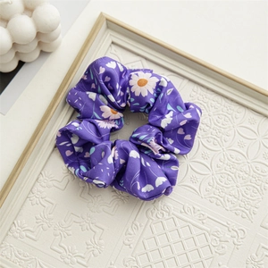 Detailed view of purple floral satin scrunchie with white daisy pattern on a relief tray