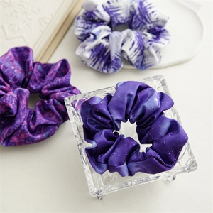 Tre elastici scrunchie in raso viola con motivi a stella, tie-dye e floreali in primo piano