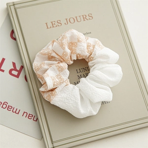 Détail macro du chouchou floral bicolore sur livre beige montrant la texture gaufrée