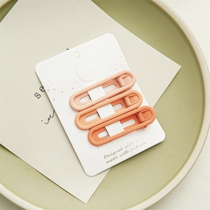 Detail view of three-piece gradient orange metal hair clips on white textured card