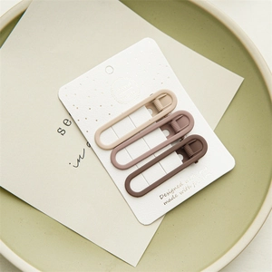 Close-up of three earth-tone matte hair clips on a card inside a ceramic dish