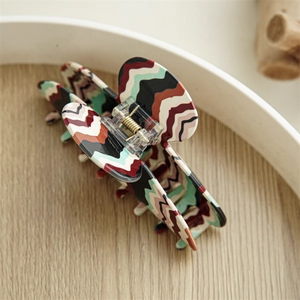 Detail of large acetate hair claw clip featuring retro wavy multi-colored stripes and gold spring