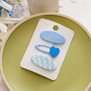 Detail of three handmade blue fabric hair clips in heart and oval shapes on a green tray