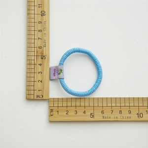 Detail view of light blue elastic hair tie with grape tag next to a measuring ruler