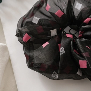 Nahaufnahme von schwarzem Haargummi aus Netzstoff mit rosa-weißen quadratischen Mustern