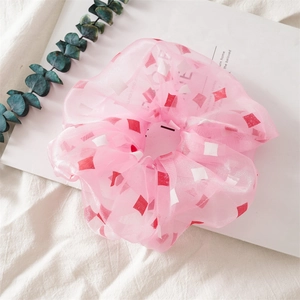 Detail eines rosa Organza-Haargummis mit Rautenmuster auf weißem Stoffhintergrund