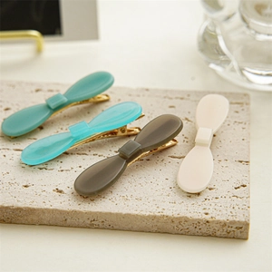 Close-up of minimalist acetate bow hair clips in four colors on a stone base