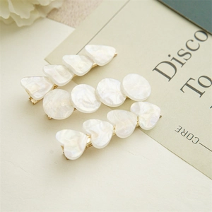 Detail view of heart, round, and triangle iridescent shell hair clips on a golden base