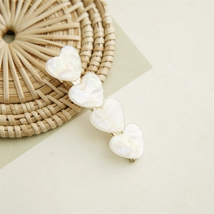 Close-up of heart-shaped shell hair clip with iridescent pearl texture on woven mat
