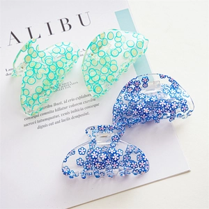 Set of four transparent acrylic hair claws with lime and floral patterns on a magazine