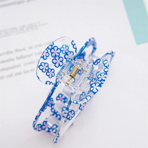 Macro view of transparent acrylic hair claw with blue floral prints and golden spring